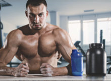 Homme musclé est assis en sueur dans la salle de gym avec un gobelet et un supplément.