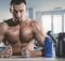 Homme musclé est assis en sueur dans la salle de gym avec un gobelet et un supplément.
